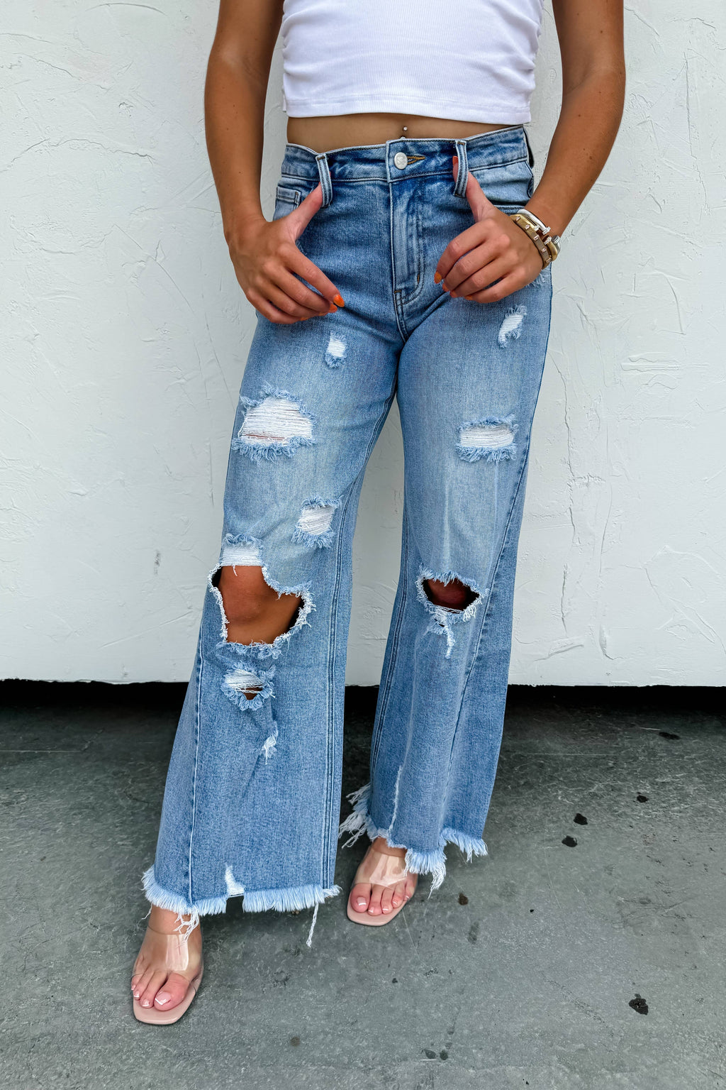 Person wearing distressed blue jeans with a white top against a white wall.