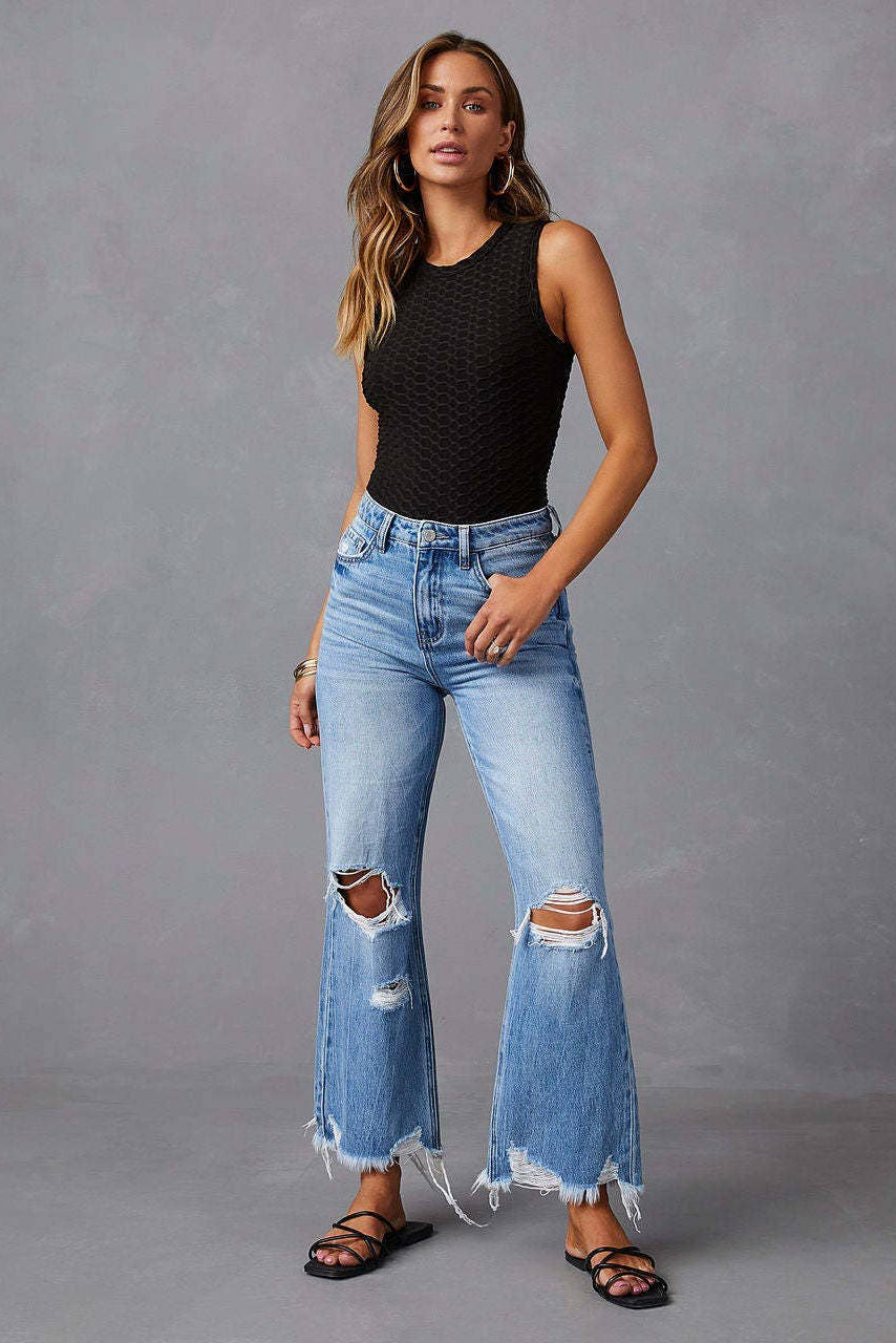 Woman wearing a black sleeveless top and blue ripped jeans against a gray background