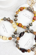 Three beaded keychains with mixed wood, metallic, and stone-like beads, displayed on white circular cards on a light fabric background.