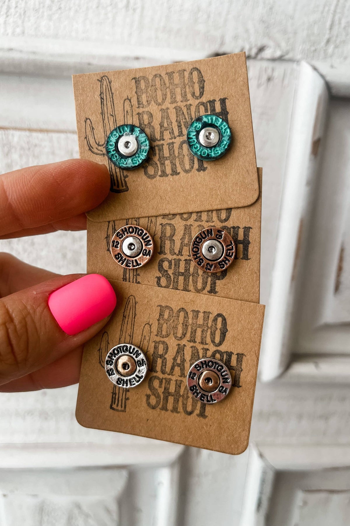Pair of earrings on a 'Boho Ranch Shop' card held by a hand with pink nail polish.