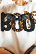 A person wearing a cream sweatshirt with a large 'BOO' graphic across the chest. The letters are black lace-textured with one in the center featuring a leopard print pattern and black bat wings, and an orange bow sits above.