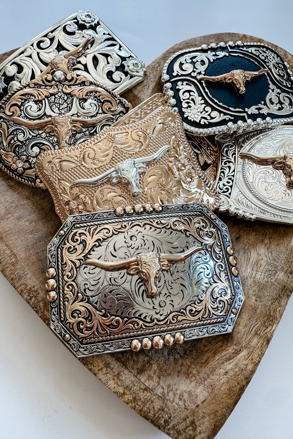 Collection of ornate belt buckles with longhorn designs on a wooden surface.