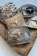Collection of ornate belt buckles with longhorn designs on a wooden surface.