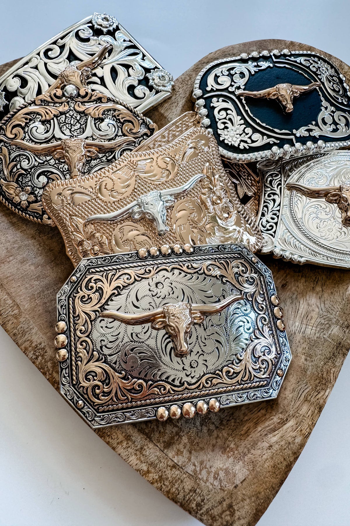Collection of ornate belt buckles with longhorn designs on a wooden surface.