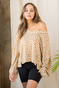Woman wearing a leopard print off-shoulder top and black shorts against a neutral wall.