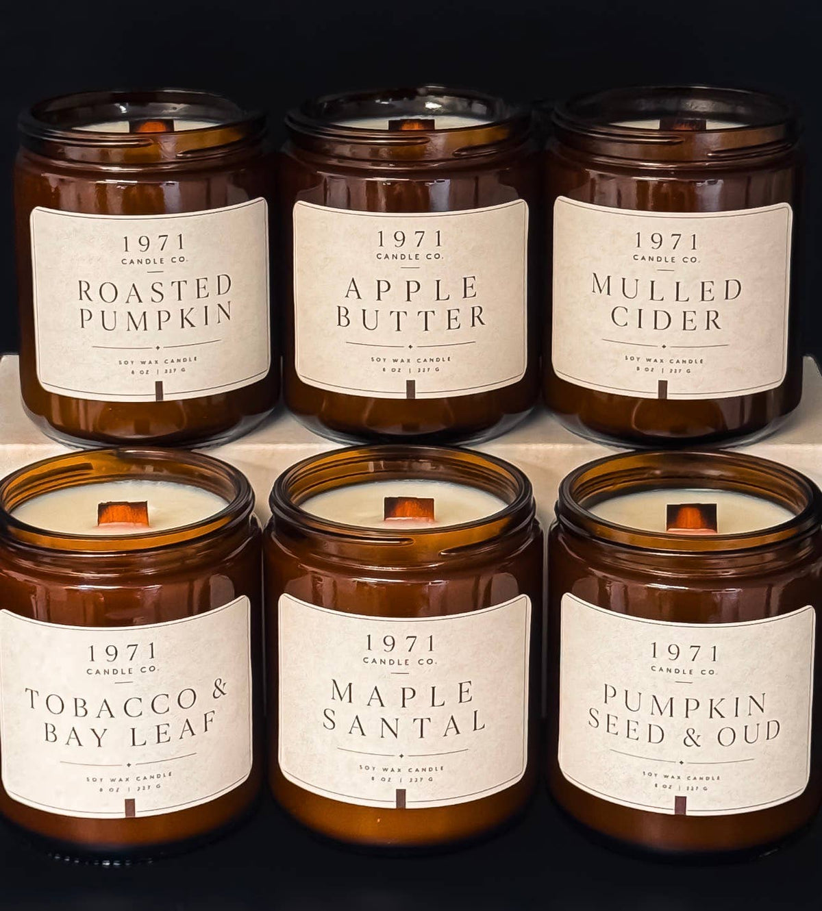 Six amber glass jar candles from 1971 Candle Co. arranged in two rows on a dark background.