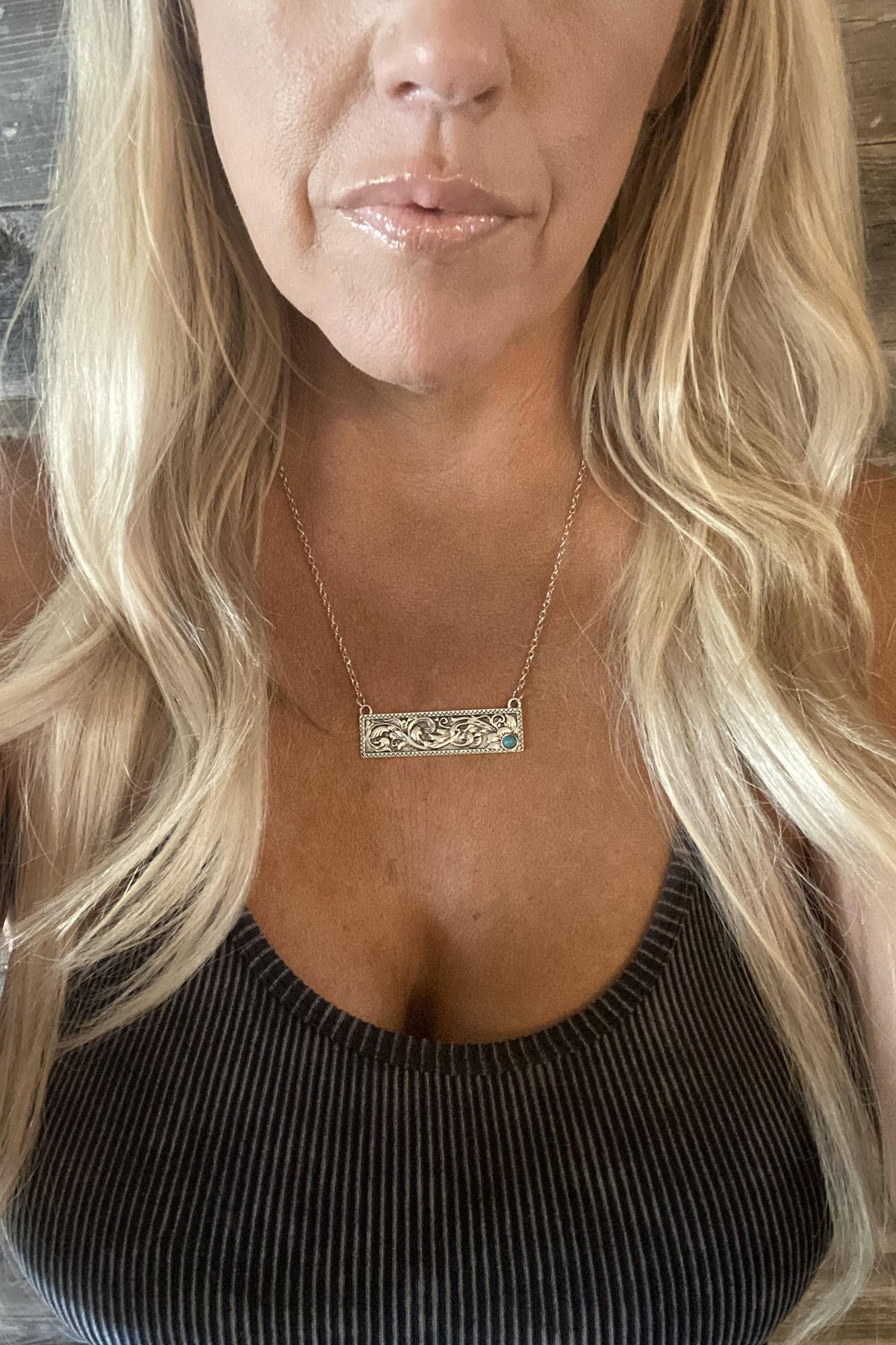 Close-up of a person wearing a gold necklace with a rectangular pendant against a wooden background