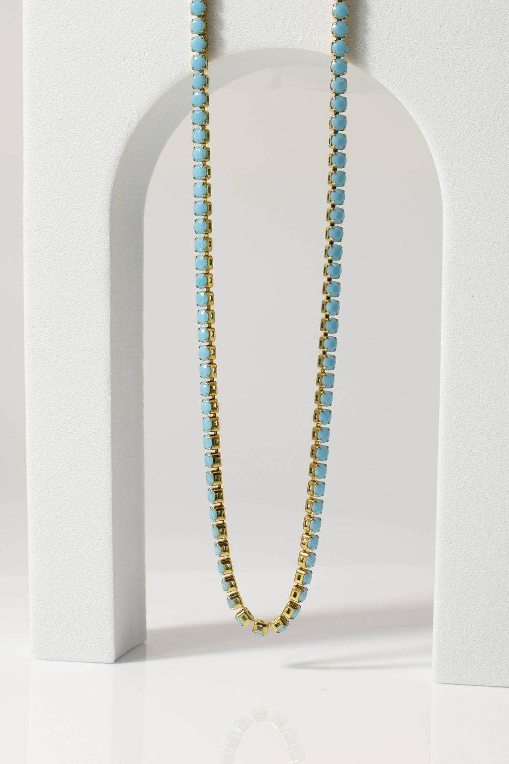 Necklace with blue beads on a white stand against a light gray background