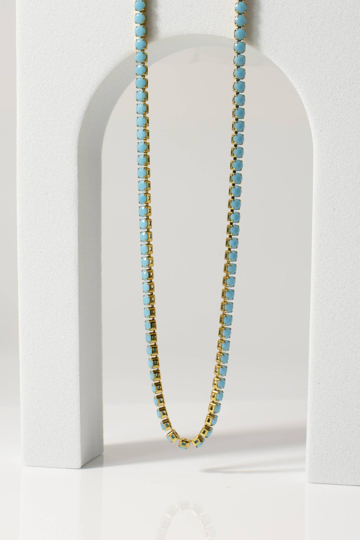 Necklace with blue beads on a white stand against a light gray background