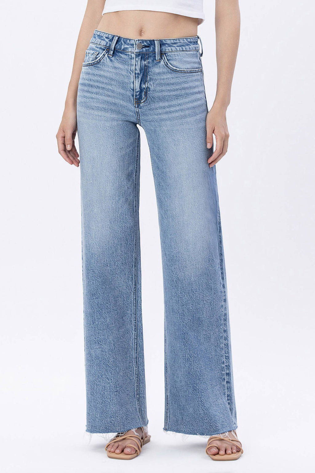 A model wearing light blue wide-leg denim jeans with a faded wash, paired with a white crop top and flat sandals, shown from the waist down on a white studio background.