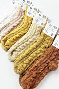 Five pairs of chunky ribbed knit socks in neutral earth tones, including cream, mustard yellow, ochre, and rust brown, arranged diagonally on a white background with decorative paper tags.