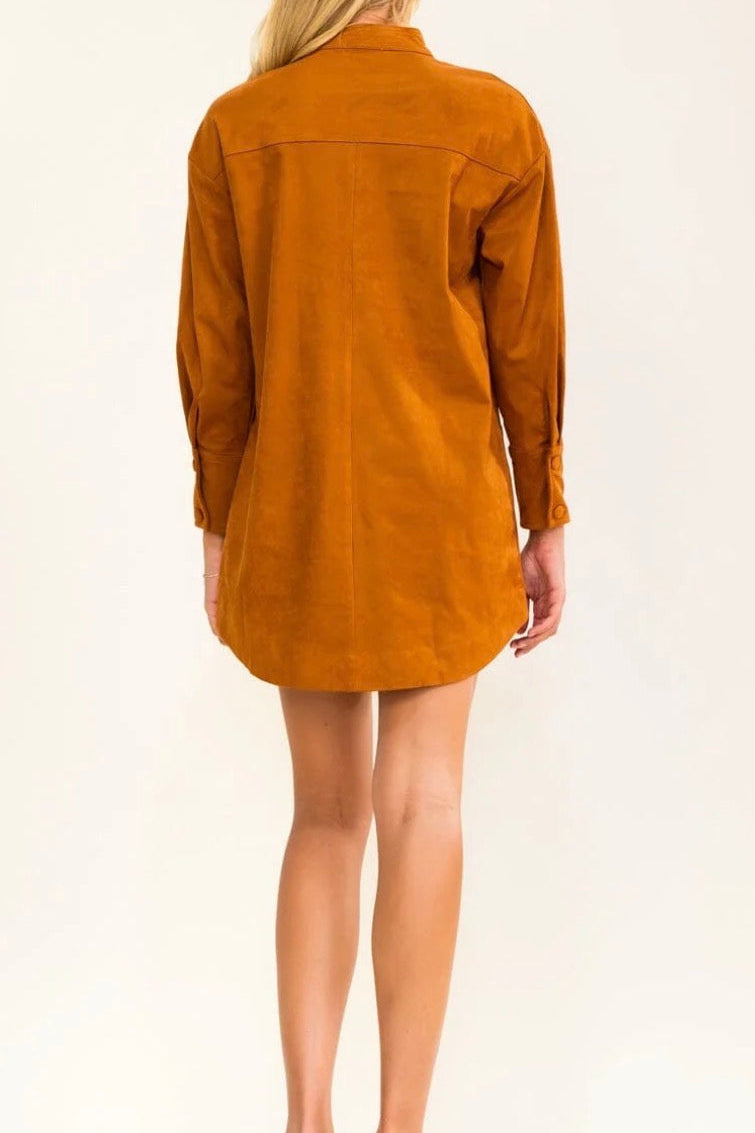 A woman viewed from the back wearing an oversized mustard orange corduroy shirt dress, paired with beige high-heeled sandals, against a plain white studio background.