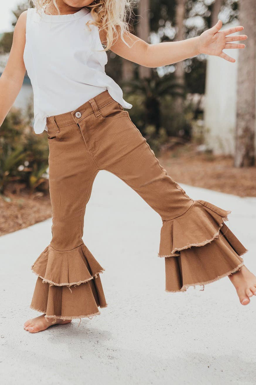 Child wearing tan ruffled pants and a white top outdoors.