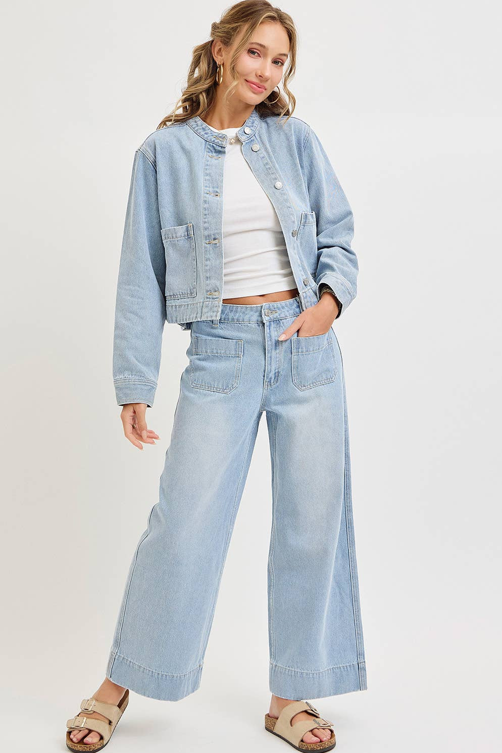 Woman wearing a light blue denim jacket and wide-leg jeans on a white background