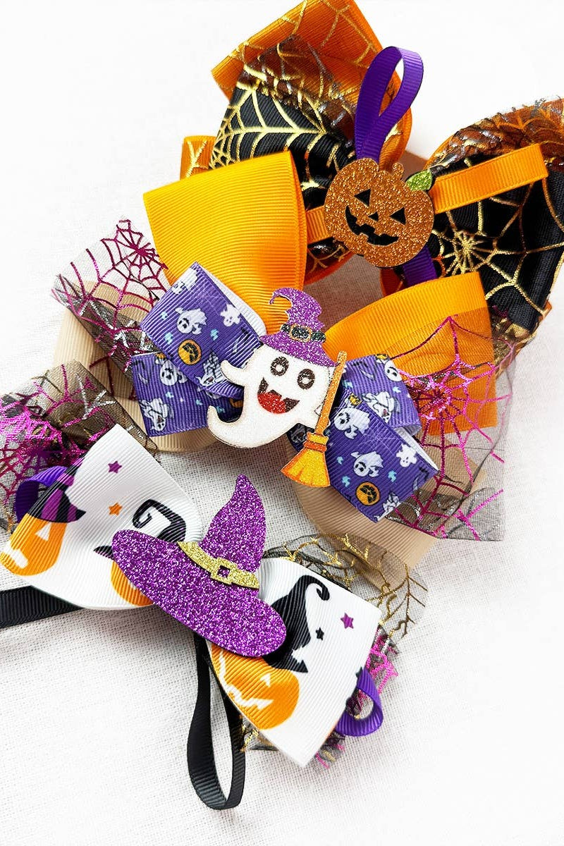 Two Halloween-themed hair bows on a white background. One bow is orange, black, and purple with spiderweb and jack-o'-lantern details.