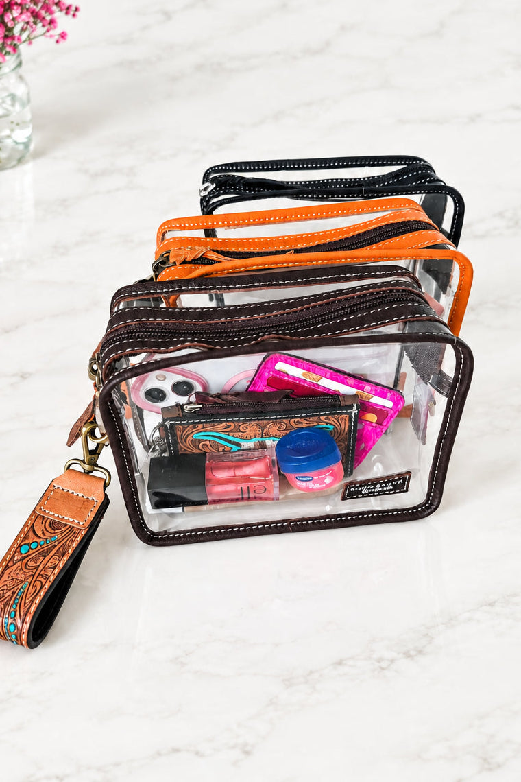 Clear makeup bag with brown leather trim containing various items on a white surface.